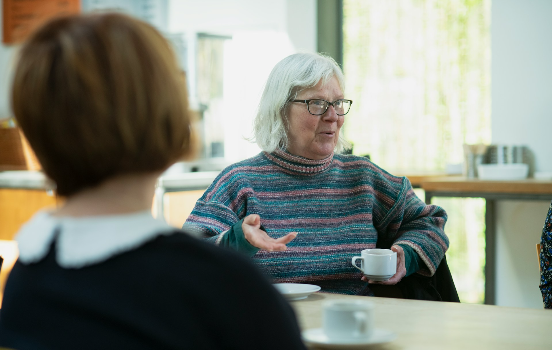 person talking to a group sat having hot drinks